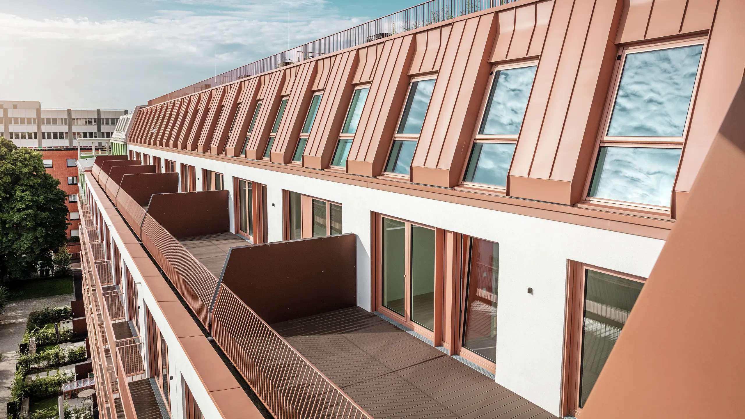 Detailansicht des modernen Dach- und Fassadendesigns des Wohnprojekts Van B in München mit dem hochwertigen PREFALZ-Aluminiumdach in IGP Orange HDP von PREFA. Die präzise Verarbeitung des langlebigen und pflegeleichten Materials gewährleistet optimalen Witterungsschutz und verleiht dem Gebäude ein einheitliches, elegantes Erscheinungsbild. Großzügige Fenster und Balkone lassen viel Tageslicht herein und schaffen einen offenen, komfortablen Wohnraum mit architektonischer Ausdruckskraft.