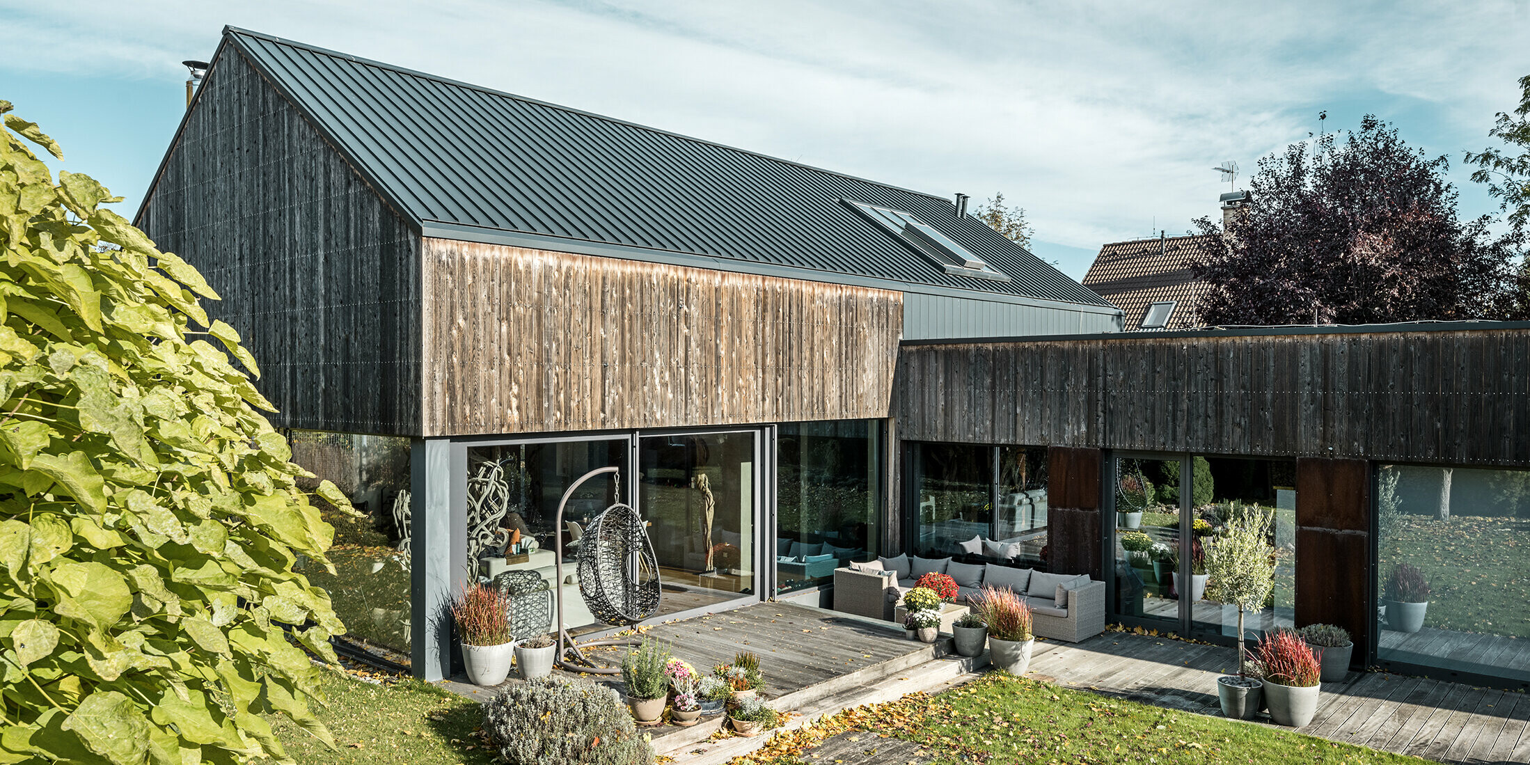 Einfamilienhaus in CZ mit Satteldach aus Aluminium. Das Dach wurde mit PREFALZ Doppelstehfalz in P.10 Anthrazit eingedeckt und mit einer Fassade aus verwittertem Zedernholz versehen. Die schöne Holzterrasse und die großzügigen Fensterflächen im Erdgeschoss unterstreichen den modernen Charakter.