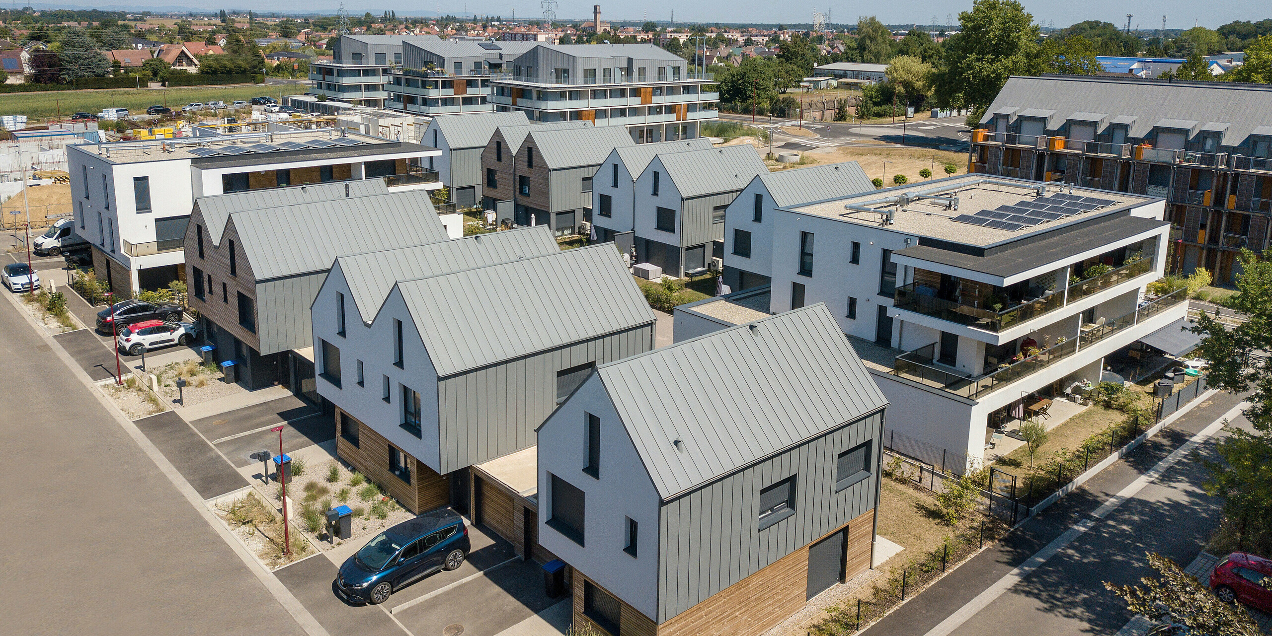 PREFALZ in Hellgrau zieht sich über die Fassaden und Satteldächer einer Reihenhaus-Siedlung in Mundolsheim. Die einheitlichen Gebäudehüllen aus Aluminium schaffen ein harmonisches Gesamtbild.