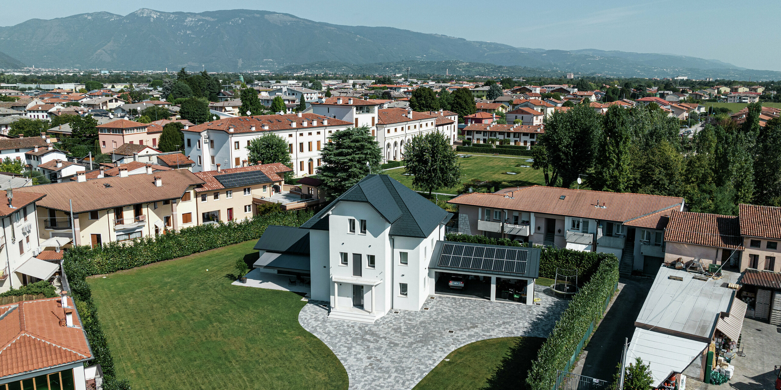 Luftaufnahme eines modernen Einfamilienhauses in Marano Vicentino, Italien, mit einem robusten Dach aus PREFA Dachschindeln in P.10 Anthrazit. Die angrenzenden Nebengebäude sind mit einer klassischen Doppelstehfalzdeckung aus Aluminium versehen. Die hochwertige Aluminiumeindeckung sorgt für eine langlebige und ästhetische Dachgestaltung.