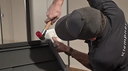 Ein Teilnehmer der Deutschen Meisterschaft im Klempnerhandwerk schlägt mit einem Hammer auf das Metall, um die Teile für eine Dachdeckung passgenau zu verbinden. Der Wettbewerb verlangt höchste Handwerkskunst und technisches Geschick.