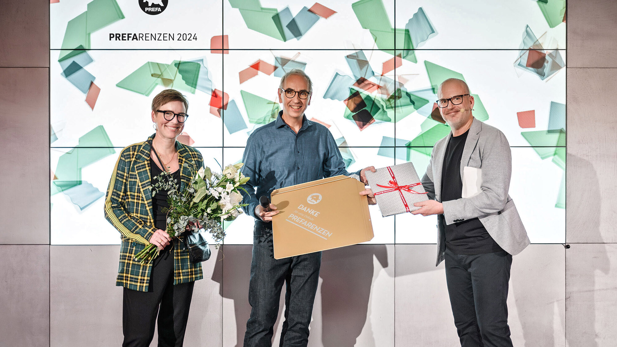 Die Fotografen Juliane Croce und Wolfgang Croce mit Marketingleiter International Jürgen Jungmair bei der Überreichung eines Geschenks vor der Präsentationsfläche.