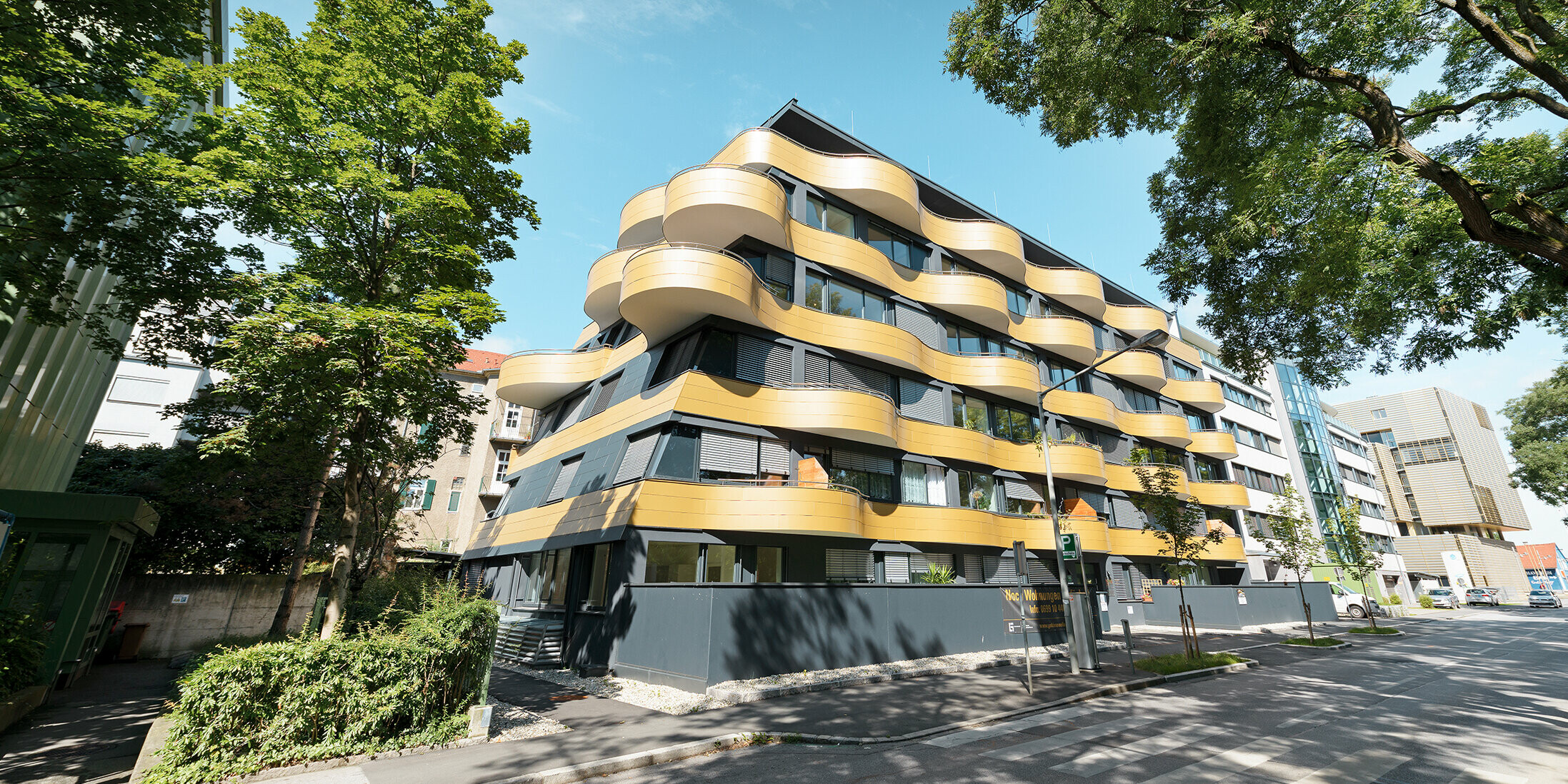 Gesamtansicht der Wohnanlage "Goldene Welle" in Graz, Österreich. Die spektakuläre Fassadengestaltung wurde mit goldfarbenen Aluminium Verbundplatten realisiert. Die runden Balkone sind Wellen nachempfunden.