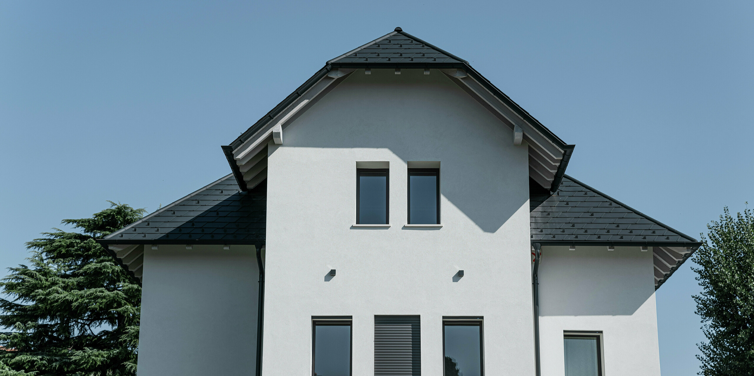 Nahaufnahme der Giebelfront eines modernen Einfamilienhauses in Marano Vicentino, Italien, mit einem PREFA Dach aus Dachschindeln in P.10 Anthrazit. Die markante Dachform und die hochwertigen Aluminiumprodukte sorgen für eine elegante und langlebige Dachlösung auf dem dreigeschossigen Gebäude.