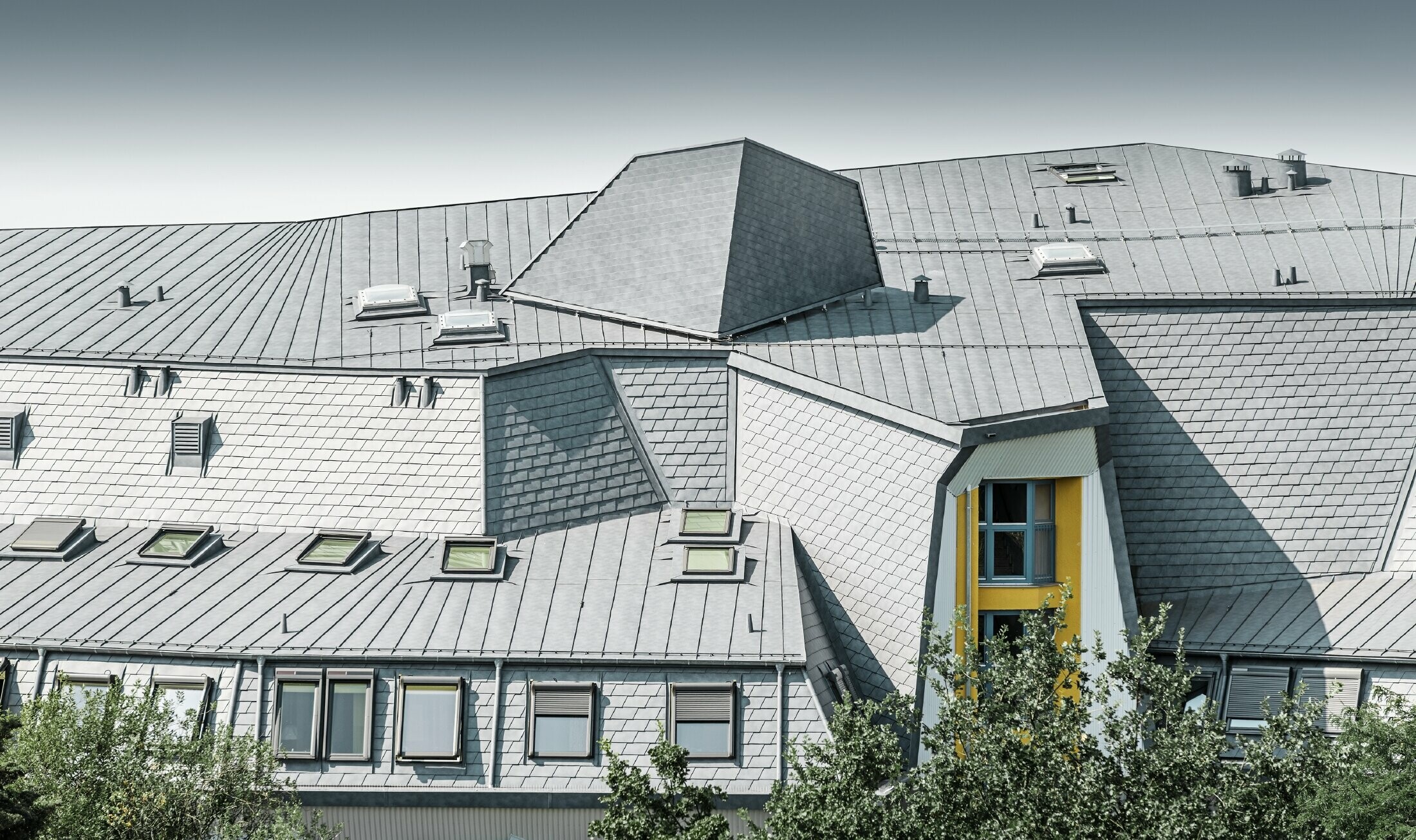 Verschachtelte Dachlandschaft mit Gauben und Verwinkelungeng am Haus Aja Textor-Goethe, eingedeckt mit der PREFA Dachschindel und Prefalz in Steingrau