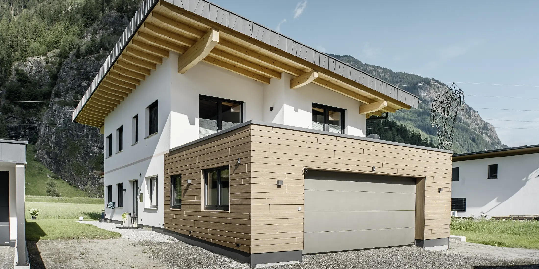 Modernes Einfamilienhaus mit Fassadensanierung: erneuerte Außenfassade mit horizontaler Fassadenverkleidung in Holzoptik, kombiniert mit weiß verputzten Flächen, integrierter Garagenverkleidung und zeitgemäßer Architektur in alpiner Umgebung.