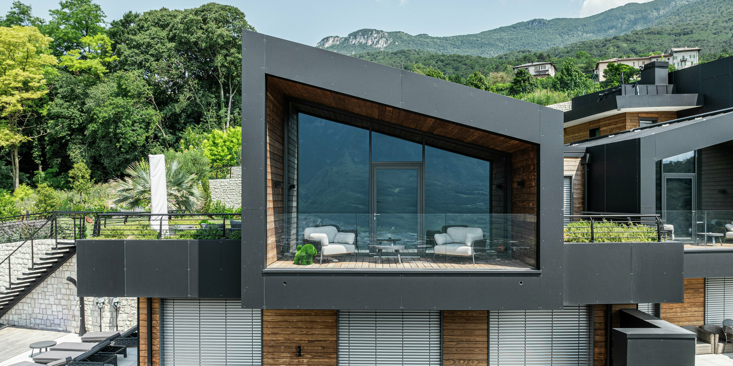 Modernes Wohnhaus mit markantem Pultdach und großflächiger Verglasung, die einen spektakulären Ausblick auf die Trientiner Berglandschaft bietet. Die Fassade aus PREFA Aluminium Verbundplatten in P.10 Schwarz sorgt für eine edle und witterungsbeständige Optik, während das warme Holz einen harmonischen Kontrast bildet. Die überdachte Loggia mit Glasgeländer verbindet Innen und Außen und bietet höchsten Wohnkomfort. Nachhaltige Materialien und langlebige PREFA Produkte garantieren Schutz, Stabilität und zeitlose Ästhetik.