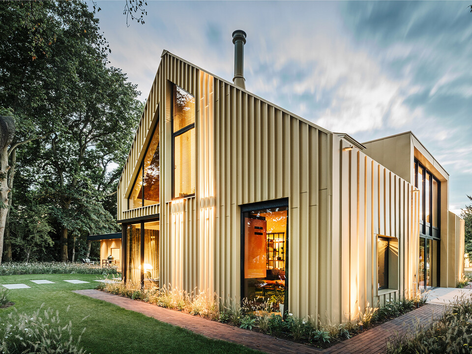 Abendaufnahme des Einfamilienhauses mit der linierten Aluminiumfassade und ausgeklügelten Außenbeleuchtung aus der seitlichen Normalperspektive.