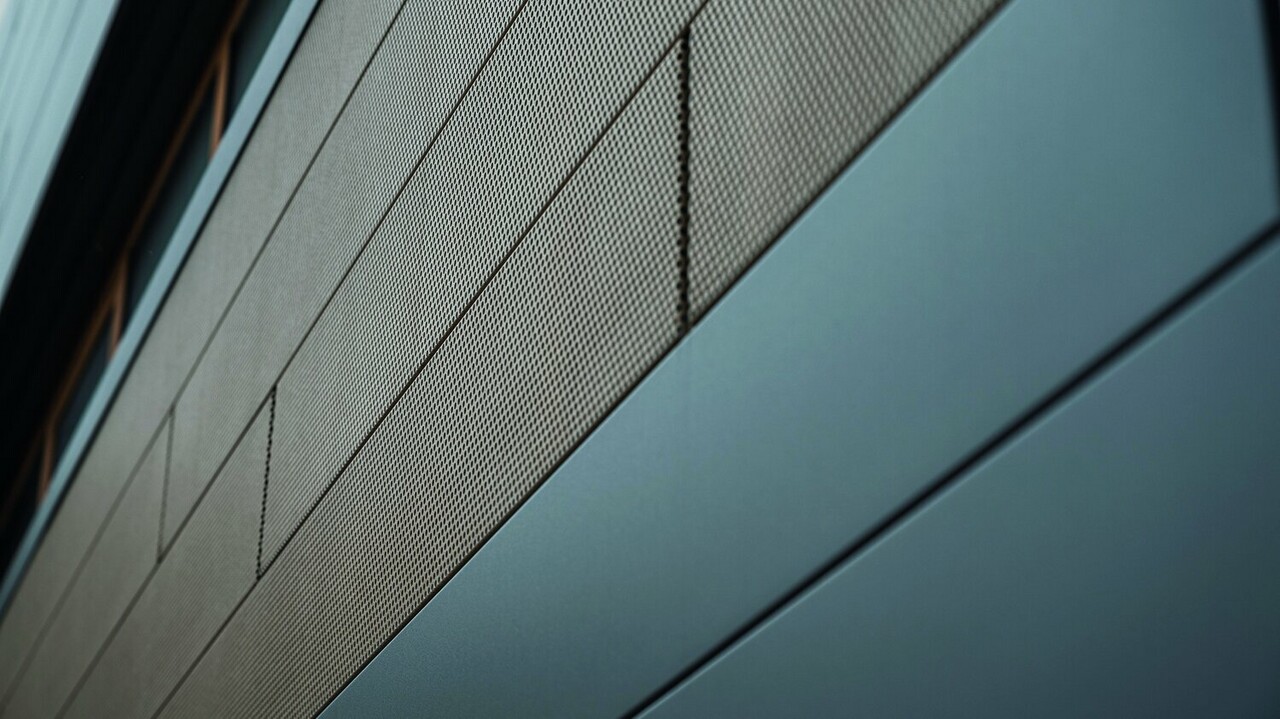 Die Fassadenpaneele von PREFA, Siding, sind jetzt auch in perforierter, also gelochter Ausführung erhältlich, hier sind sandbraune gelochte Elemente mit grauen Paneelen kombiniert. 