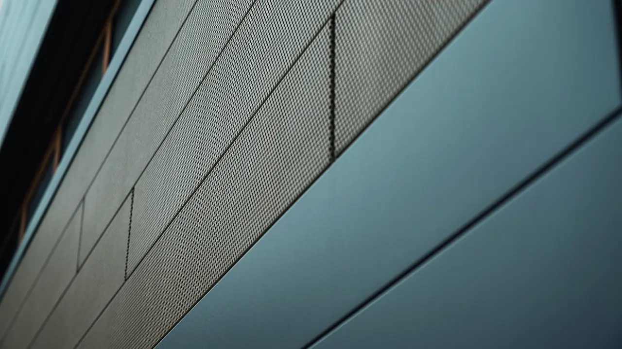Die Fassadenpaneele von PREFA, Siding, sind jetzt auch in perforierter, also gelochter Ausführung erhältlich, hier sind sandbraune gelochte Elemente mit grauen Paneelen kombiniert. 