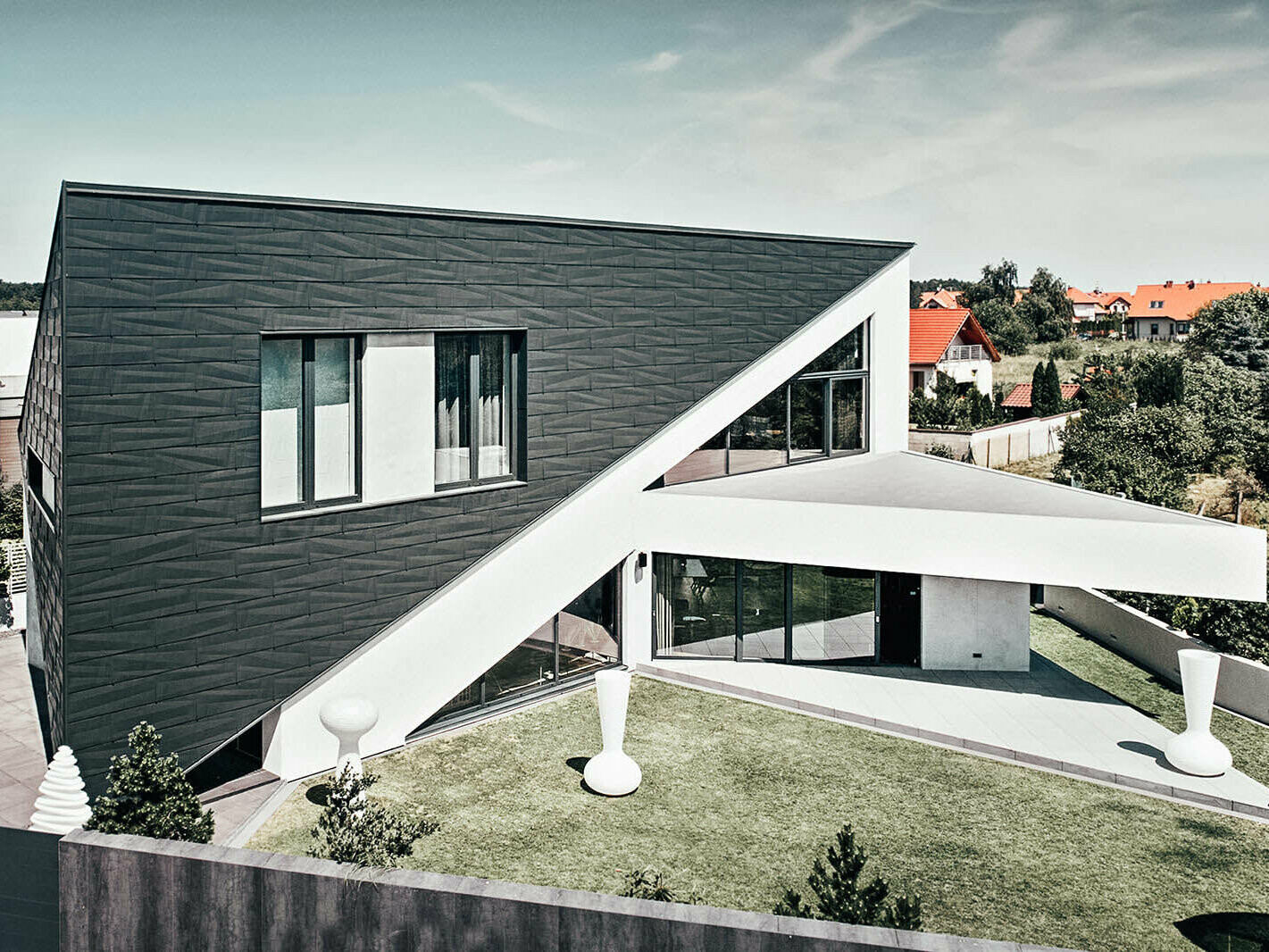 Seitliche Ansicht des Dreieckshauses in Polen. Es ist mit PREFA Siding.X Fassadenelementen verkleidet, die zum weißen Kontrast des restlichen Hauses passen.