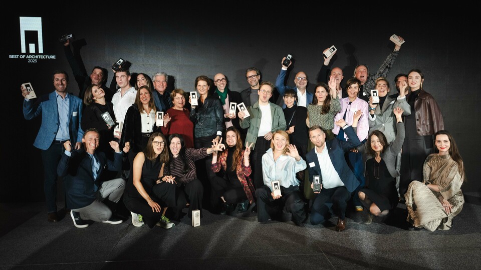 Gruppenfoto der Gewinner bei der Preisverleihung „Wohngebäude des Jahres 2025“: Die Gewinner stehen vor einer eleganten schwarzen Bühne mit dem Logo „Best of Architecture“ und halten stolz ihre Auszeichnungen in den Händen. Dynamische Posen, moderne Kleidung und auffällige Beleuchtung unterstreichen die Bedeutung der Veranstaltung, während die Bühne für Innovation und architektonische Exzellenz steht.