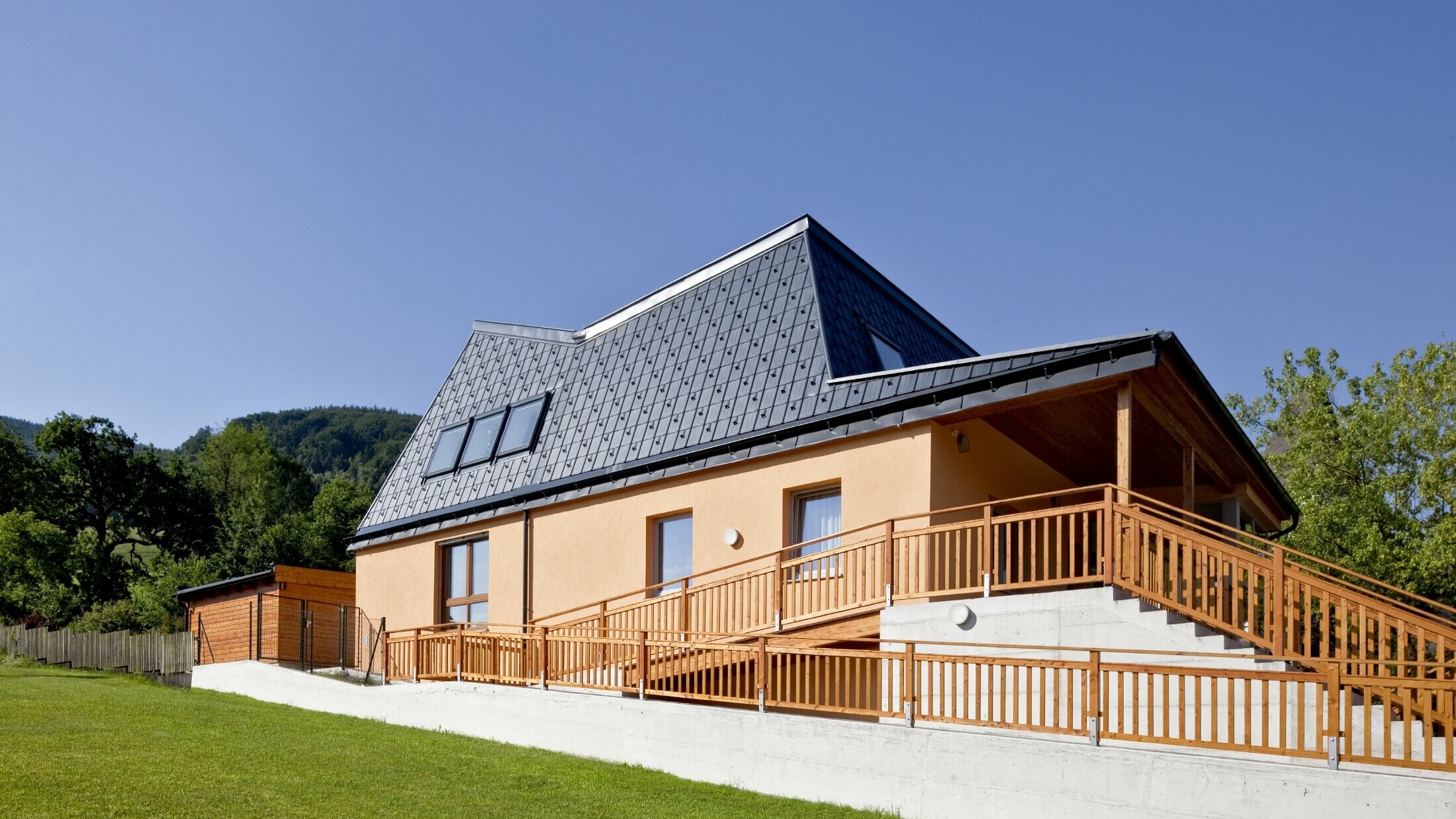 Kindergarten mit oranger Putzfassade und verwinkeltem Dach, gedeckt mit der PREFA Dachplatte in P.10 Anthrazit;