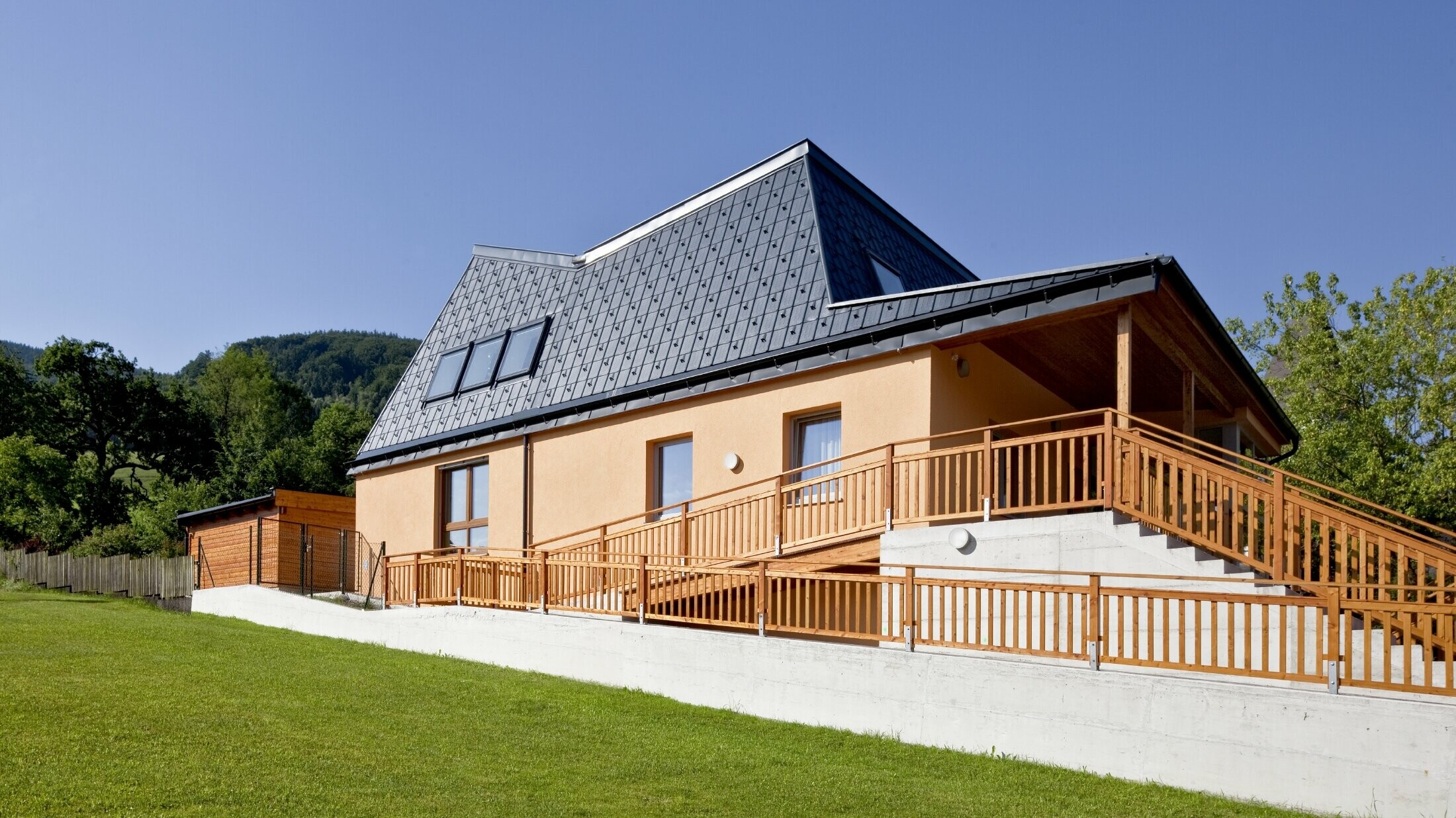 Kindergarten mit oranger Putzfassade und verwinkeltem Dach, gedeckt mit der PREFA Dachplatte in P.10 Anthrazit;