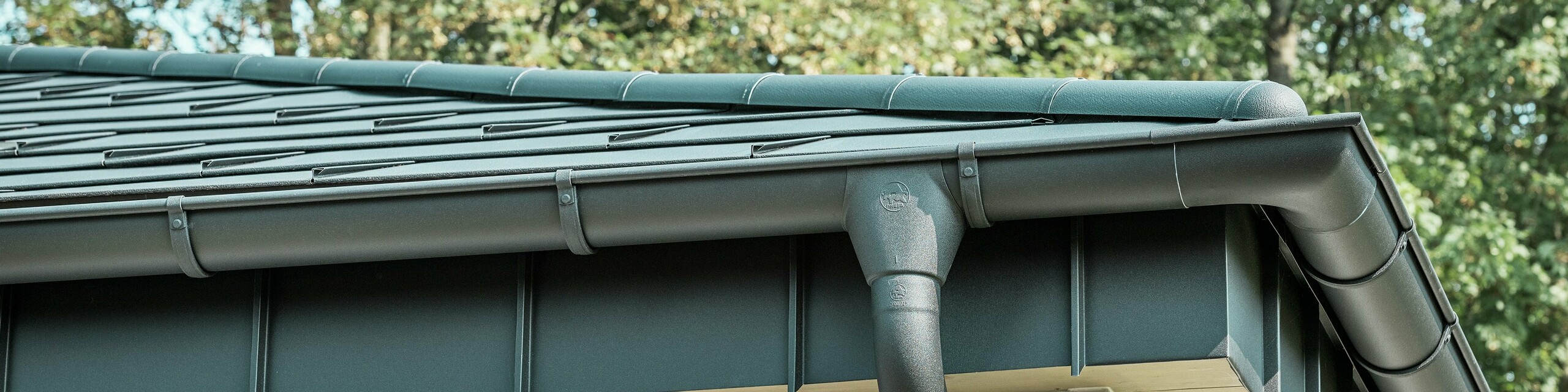 Detailansicht der PREFA Dachentwässerung eines Bungalows in Rommerskirchen. Die hochwertige Saumrinne und das Ablaufrohr in P.10 Schwarz bieten eine sichere Dachentwässerung bei Regen. Die langlebigen PREFA Aluminiumprodukte verbinden Funktionalität mit modernem, elegantem Design.