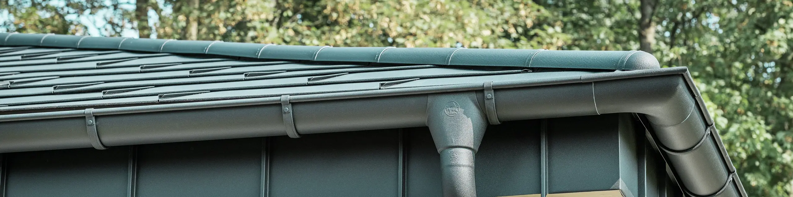 Detailansicht der PREFA Dachentwässerung eines Bungalows in Rommerskirchen. Die hochwertige Saumrinne und das Ablaufrohr in P.10 Schwarz bieten eine sichere Dachentwässerung bei Regen. Die langlebigen PREFA Aluminiumprodukte verbinden Funktionalität mit modernem, elegantem Design.