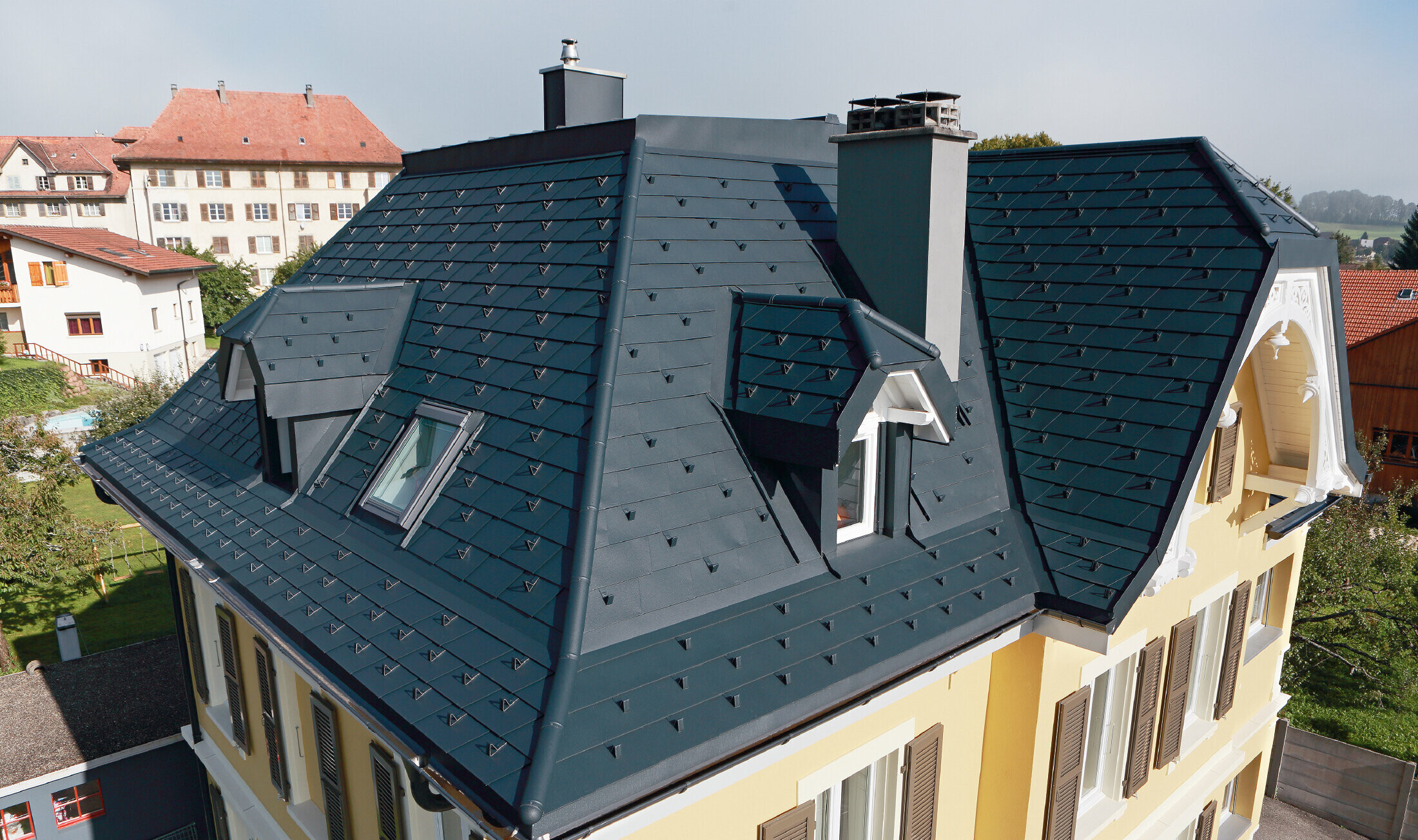 Villa in der Schweiz, das Dach hat viele Kehlen und kleine Gauben, das Dach ist mit einer Alu Schindel von PREFA eingedeckt in P.10 Anthrazit