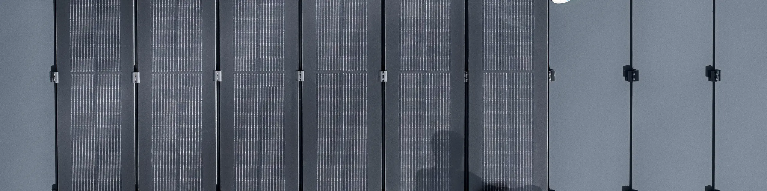 Zwei Personen installieren PREFALZ-Solarmodule auf einer großen grauen Dachfläche, die mit doppelflanschigen Paneelen bedeckt ist.