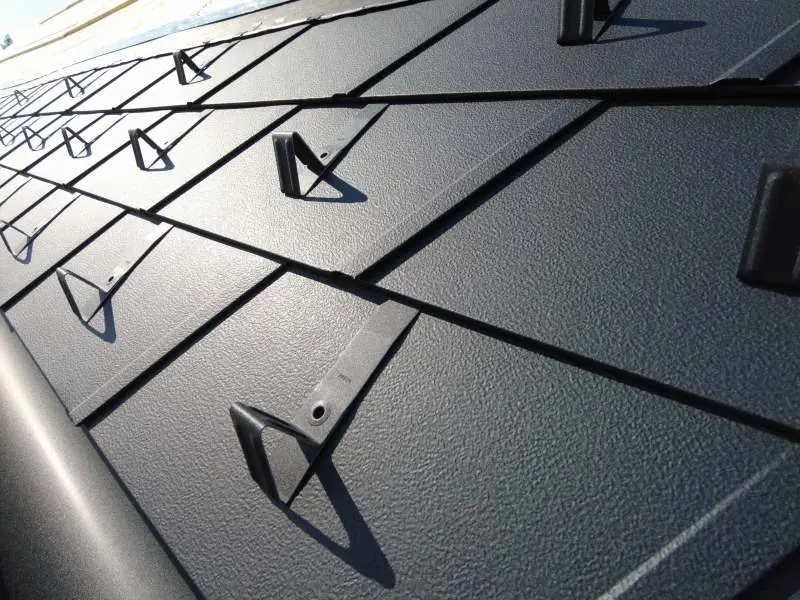 Detailaufnahme der Dachschindel DS.19 in der Farbe P.10 Anthrazit bei Sonnenschein. Zudem wurden Schneestopper montiert.