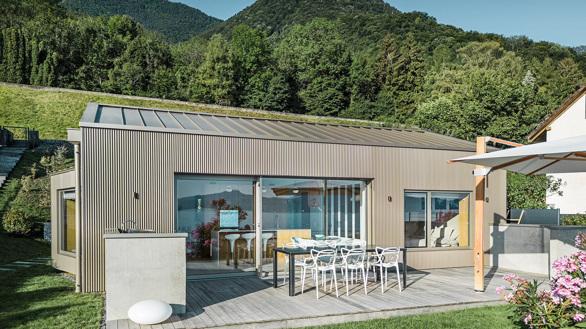 Seitliche Ansicht des Seehauses mit Blick auf die Terrasse und einer bergigen Landschaft im Hintergrund.