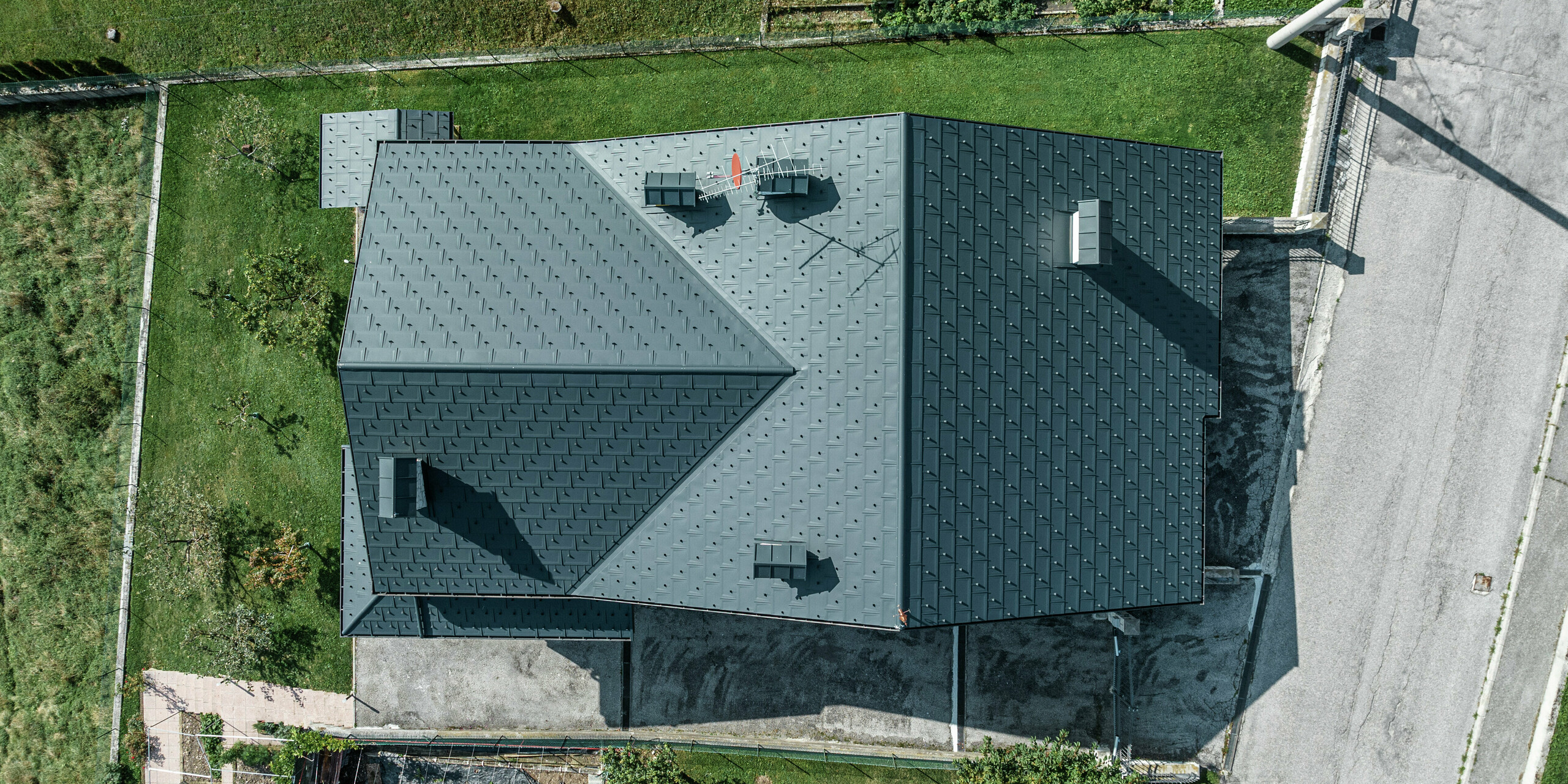 Drohnenaufnahme eines Einfamilienhauses in Gallio mit hochwertiger PREFA Dacheindeckung aus Dachplatten R.16 in P.10 Dunkelgrau. Die Aluminium-Dachlösung überzeugt durch moderne Optik, extreme Witterungsbeständigkeit und Langlebigkeit. Schneestopper sorgen für zusätzliche Sicherheit in alpinen Regionen. Die präzise Verarbeitung und das durchdachte Entwässerungssystem garantieren optimalen Schutz vor Regen und Schnee. Ein wartungsarmes Dach für Generationen.