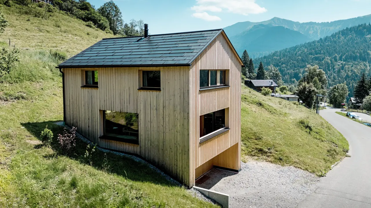 Hoch über dem Tal steht Haus Immi wie ein klarer Holzmonolith im sonnigen Berghang von Ebnit. Die reduzierte Weißtannenfassade und das schwarze PREFA Solardach setzen einen kraftvollen Kontrast zur weiten Alpenlandschaft. Integrierte Solardachplatten und Dachplatten R.16 in P.10 Schwarz liefern Solarstrom, trotzen alpinem Wetter und sichern ein langlebiges, harmonisches Dachbild.