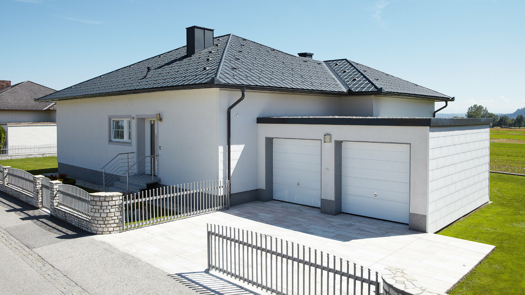 Der neugebaute Bungalow mit Zeltdach wurde mit der PREFA Dachplatte in P.10 Anthrazit eingedeckt. Rechts daneben wurde eine Doppelgarage angebaut, fotografiert wurde von der Straße aus.