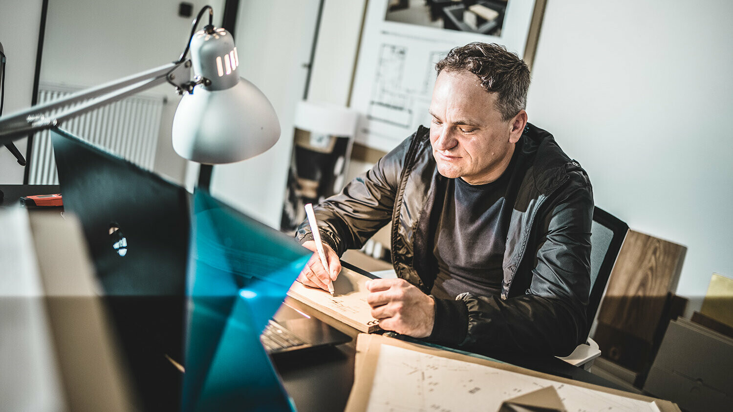 Portrait von Daniel Zerzán in seinem Büro, sein Blick ist auf den vor ihm liegenden Notizblock ausgerichtet, auf dem er gerade schreibt. 