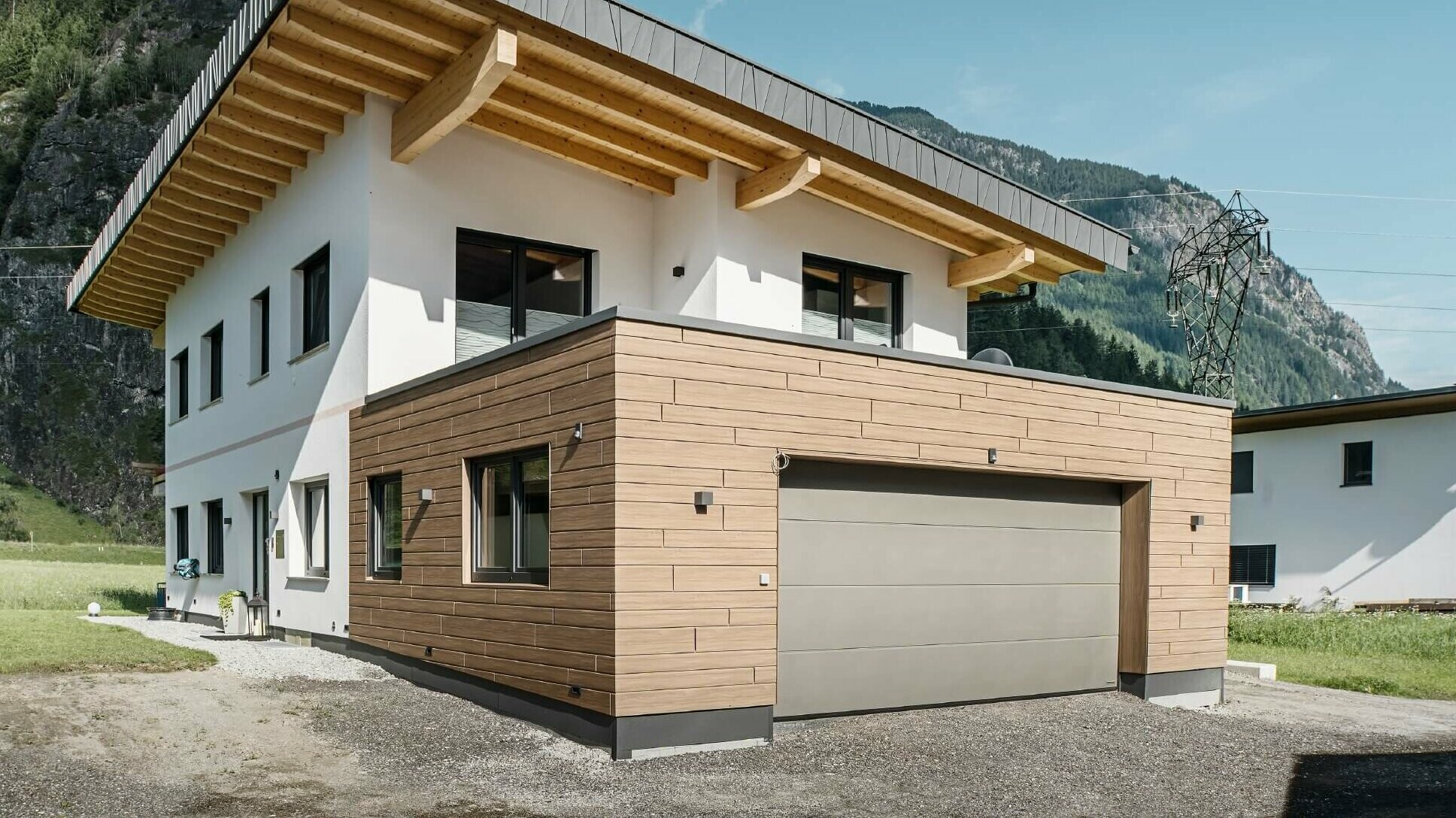Garage eines Wohnhauses mit PREFA Sidings in Holzoptik im Farbton "Walnuss Braun". Im Hintergrund sind Berge zu sehen. 