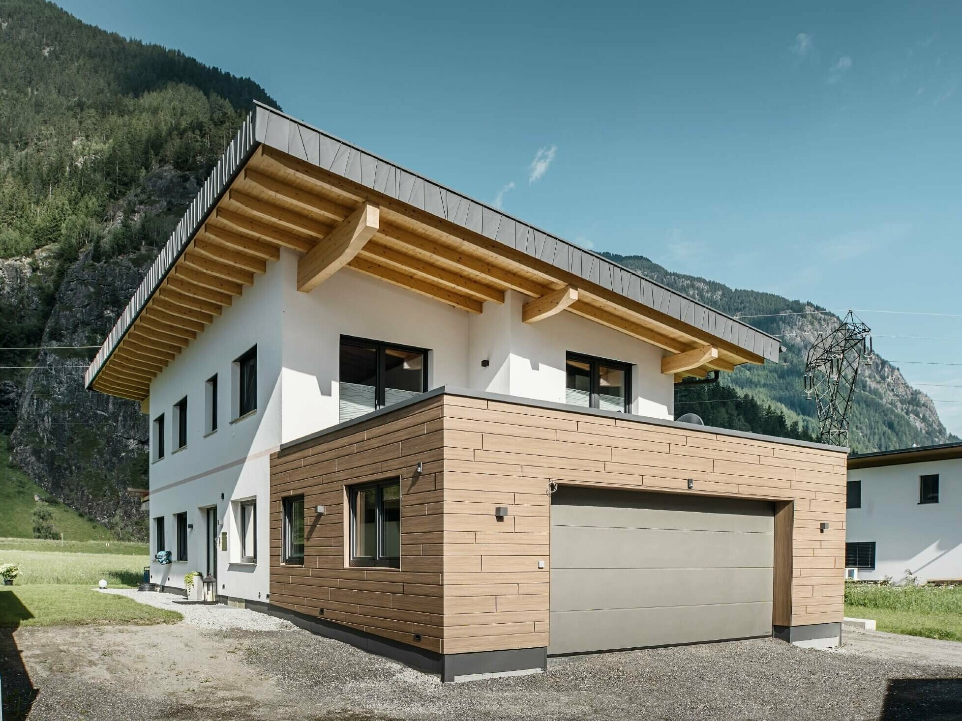 Garage eines Wohnhauses mit PREFA Sidings in Holzoptik im Farbton "Walnuss Braun". Im Hintergrund sind Berge zu sehen. 