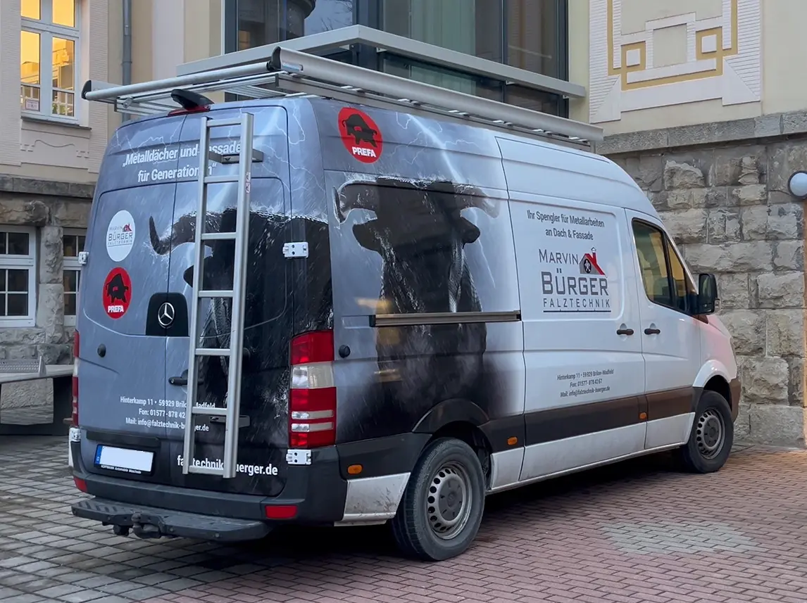 Der Sprinter von Marvin Bürger steht vor der Regelschule am Pulverrasen in Meiningen. Auf dem Fahrzeug sind das PREFA-Logo sowie das Logo von Falztechnik Bürger abgebildet. Der Sprinter ist mit einer auffälligen Werbung für Marvin Bürger und seine Dienstleistungen im Bereich Metallarbeiten an Dach und Fassade bedruckt.