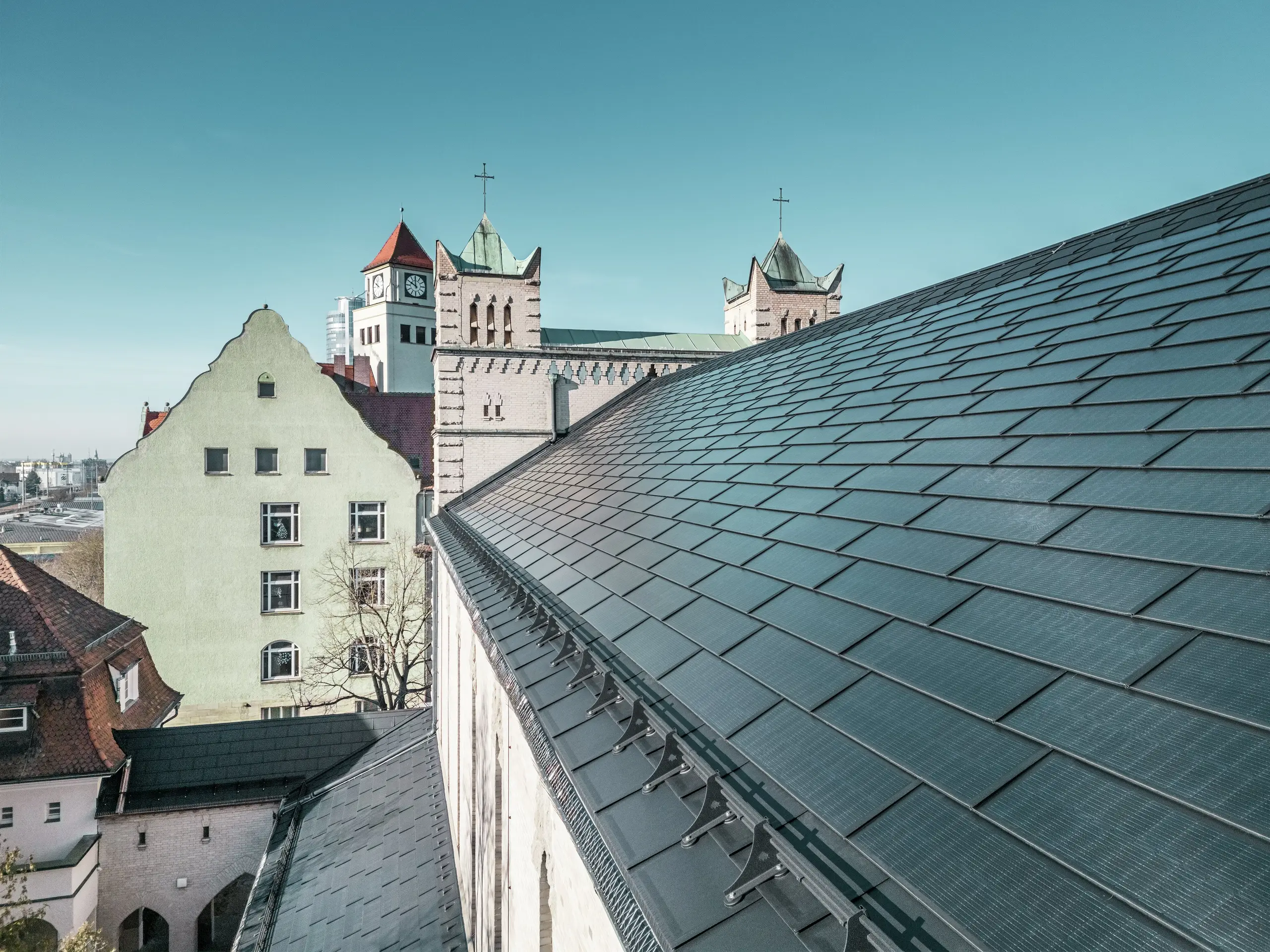 Die Nahaufnahme des Daches der St. Karl Borromäus Kirche in Nürnberg zeigt die präzise verlegten PREFA Solardachplatten in elegantem Schwarz. Die gut integrierten Solarmodule fügen sich harmonisch in die historische Architektur ein und stellen eine nachhaltige Energiequelle dar. Im Hintergrund sind die markanten Kirchtürme mit ihren klassischen spitzen Dächern zu sehen. Die PREFA Dachlösung aus robustem Aluminium verbindet Denkmalschutz mit erneuerbarer Energie perfekt.