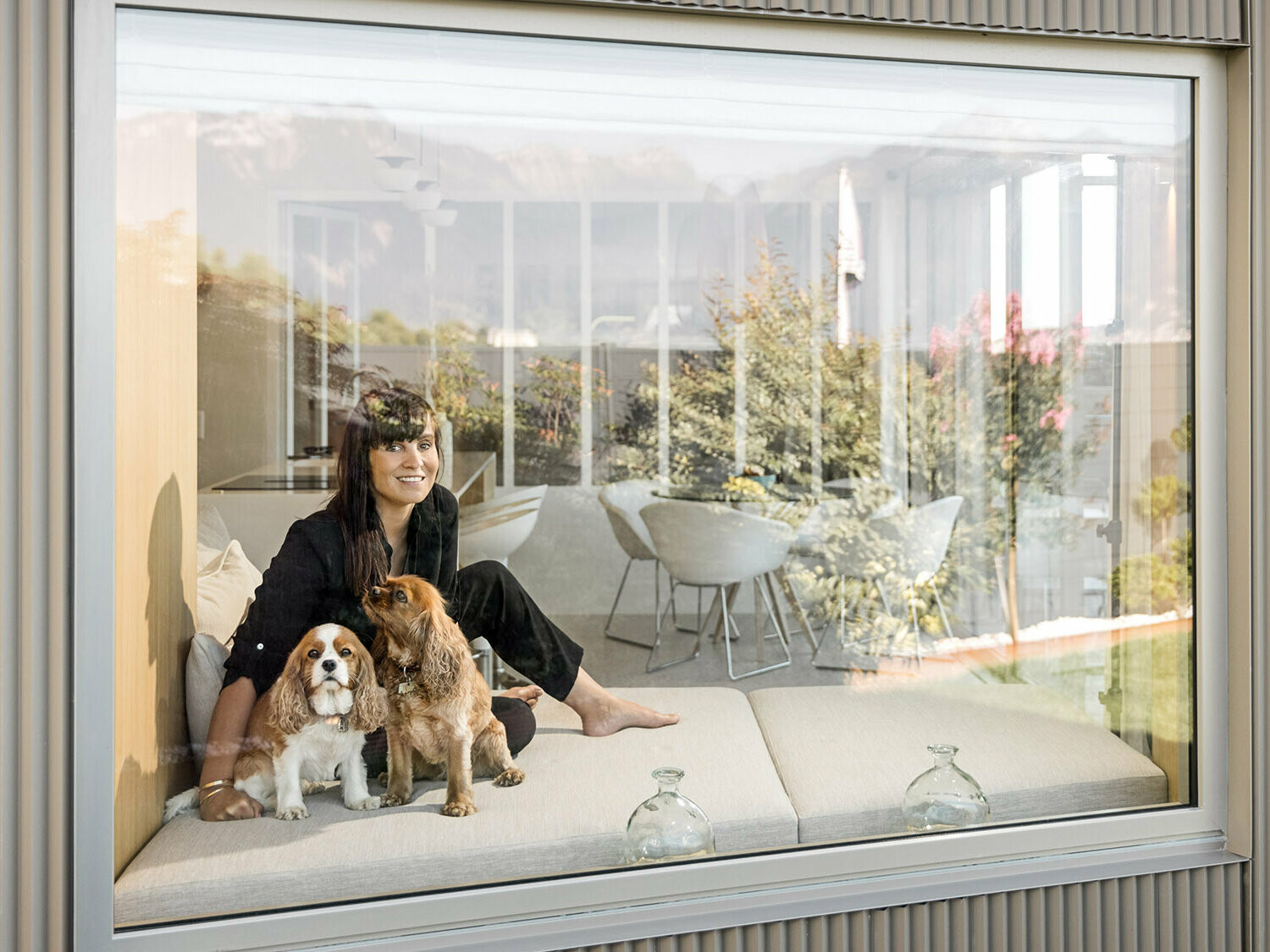 Portrait von Sophie Morard, die mit ihren beiden Hunden hinter dem Fenster in ihrem Seehaus sitzt.
