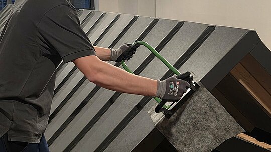 Ein Teilnehmer der Deutschen Meisterschaft im Klempnerhandwerk verwendet einen Winkelfalzschließer, um eine Dachplatte präzise zu bearbeiten.