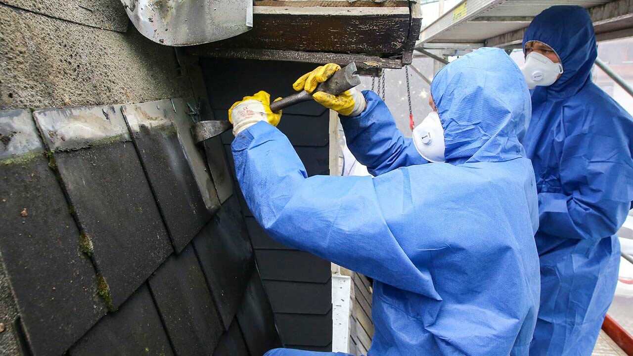 Abtragen der asbesthaltigen Faserzementplatten durch die mit blauen Schutzanzügen ausgestatteten Profis