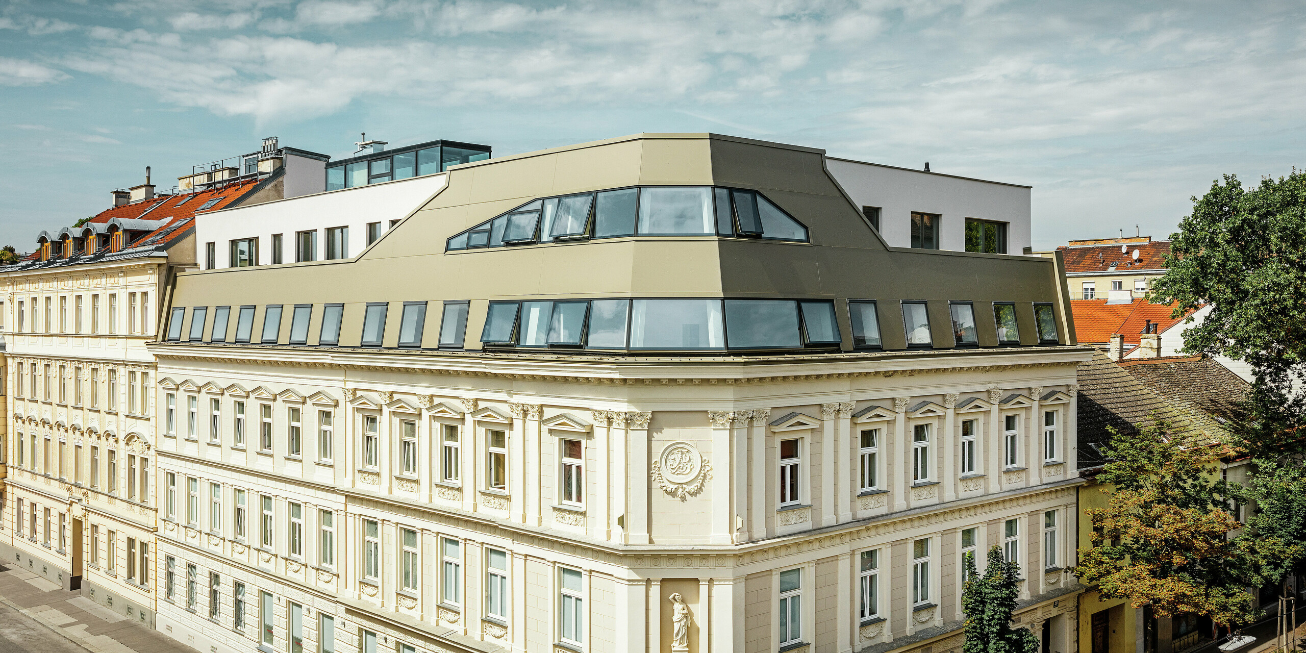 Gesamtansicht des Dachflächenausbaus in der Schloßhofer Straße in Wien mit der Aluminium Verbundplatte in Bronze. Der komplette Dachausbau des historischen Gebäudes in Wien überzeugt durch die harmonische Kombination von Glas und PREFA Aluminium Verbundplatten in Bronze. Selbstbewusst, aber stilvoll schmiegt sich die neue Architektur an den klassizistischen Bestand.