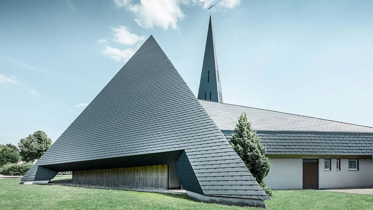 Kirche Langenau in Form einer Pyramide mit einem neuen sturmsicheren Aluminium Dach von PREFA, mit grüner Wiese und blauem Himmel und vereinzelten Wolken