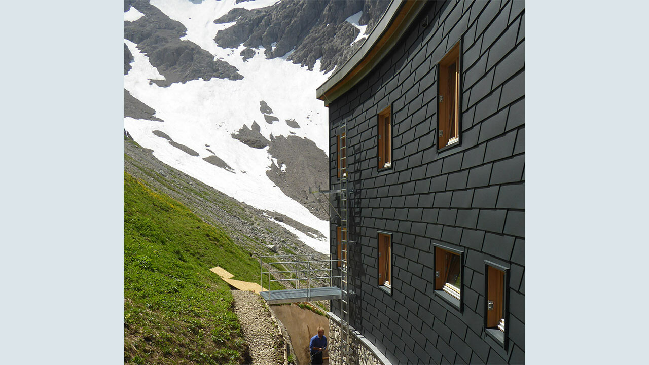 Das Waltenberger Haus in den Allgäuer Alpen wurde neu gebaut, auf der Rückseite, der Berg zugewandten Seite, wurde die robuste Wandschindel von PREFA in Anthrazit verlegt.