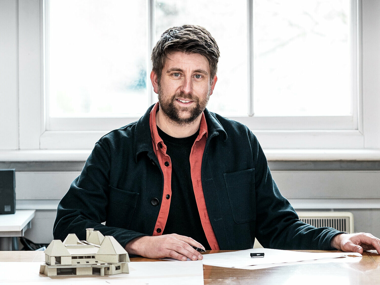 Portrait des leitenden Architekten Tim Howell vom britischen Büro Mitchell Evans Architects, vor einem Modell an einem Tisch sitzend.