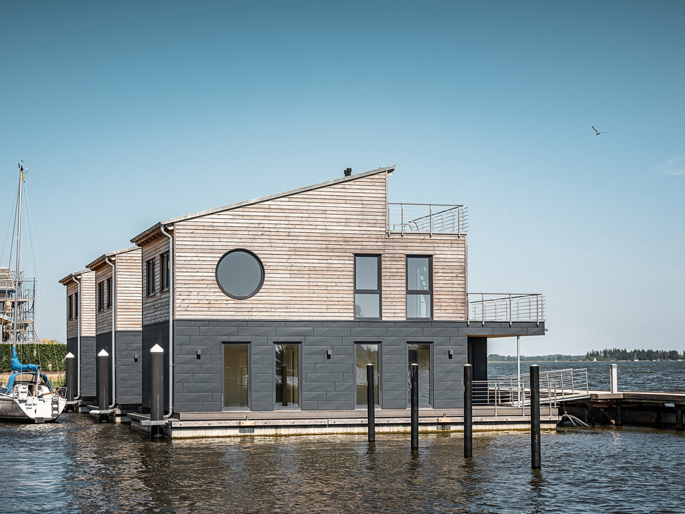 Seitlicher Blick auf drei der mit Holz und Aluminium ummantelten "schwimmenden Häuser" im Pionierhafen Schleswig.