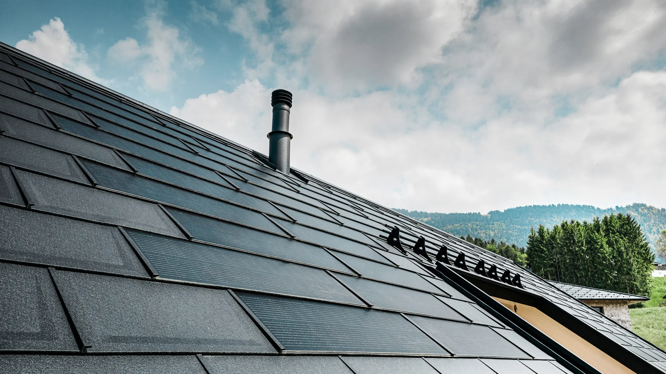 Detailansicht der PREFA Solardachplatte kombiniert mit der bewährten PREFA Dachplatte R.16 in der Farbe P.10 Schwarz auf einem Ökohaus in Egg, Österreich. Die integrierten Photovoltaikmodule zeigen die nahtlose Verbindung von erneuerbarer Energie und anspruchsvollem Dachdesign. Die schwarzen Dachplatten R.16 mit dem Schneeschutzsystem runden die ästhetische Dachoberfläche ab sorgen zudem für Sicherheit.