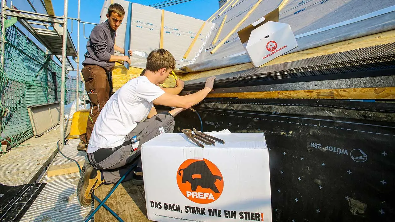 die Klempner der Firma Schütz bei der Arbeit, sie montieren den PREFA Saumstreifen für die Dachschindel, im Vordergrund steht ein PREFA Karton