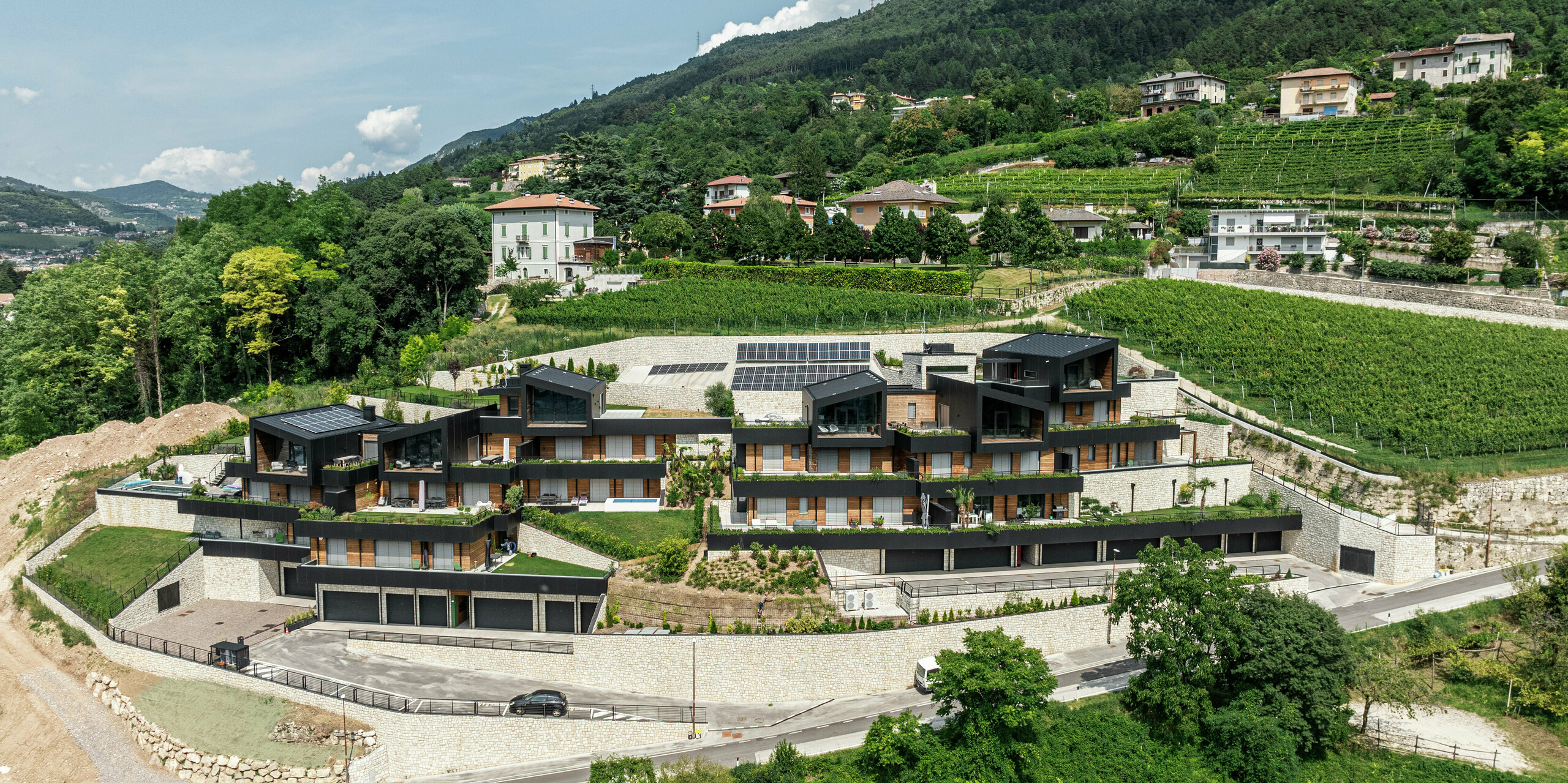Perfekte Symbiose aus Natur und moderner Architektur: Die exklusive Wohnanlage in Hanglage fügt sich harmonisch in die umliegenden Weinberge von Trento ein. Die Fassaden aus PREFA Aluminium Verbundplatten in P.10 Schwarz und die PREFALZ Dächer bieten nicht nur ein stilvolles Design, sondern auch höchste Witterungsbeständigkeit. Grünflächen, Photovoltaikanlagen und großzügige Terrassen unterstreichen das nachhaltige Wohnkonzept. Die Kombination aus Naturstein, Holz und Aluminium schafft eine langlebige, pflegeleichte Gebäudehülle mit einzigartigem Panoramablick über das Tal.