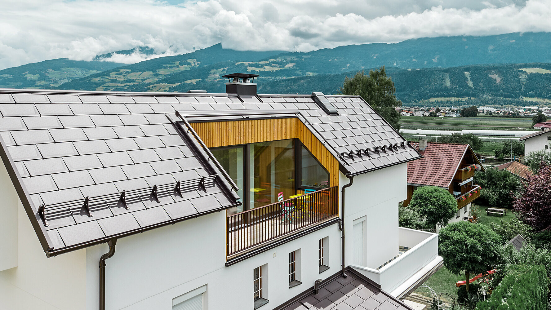 Wohnhaus eingedeckt mit der Aluminium Dachplatte R.16 in Nussbraun von PREFA mit großem Balkon und heller Putzfassade.