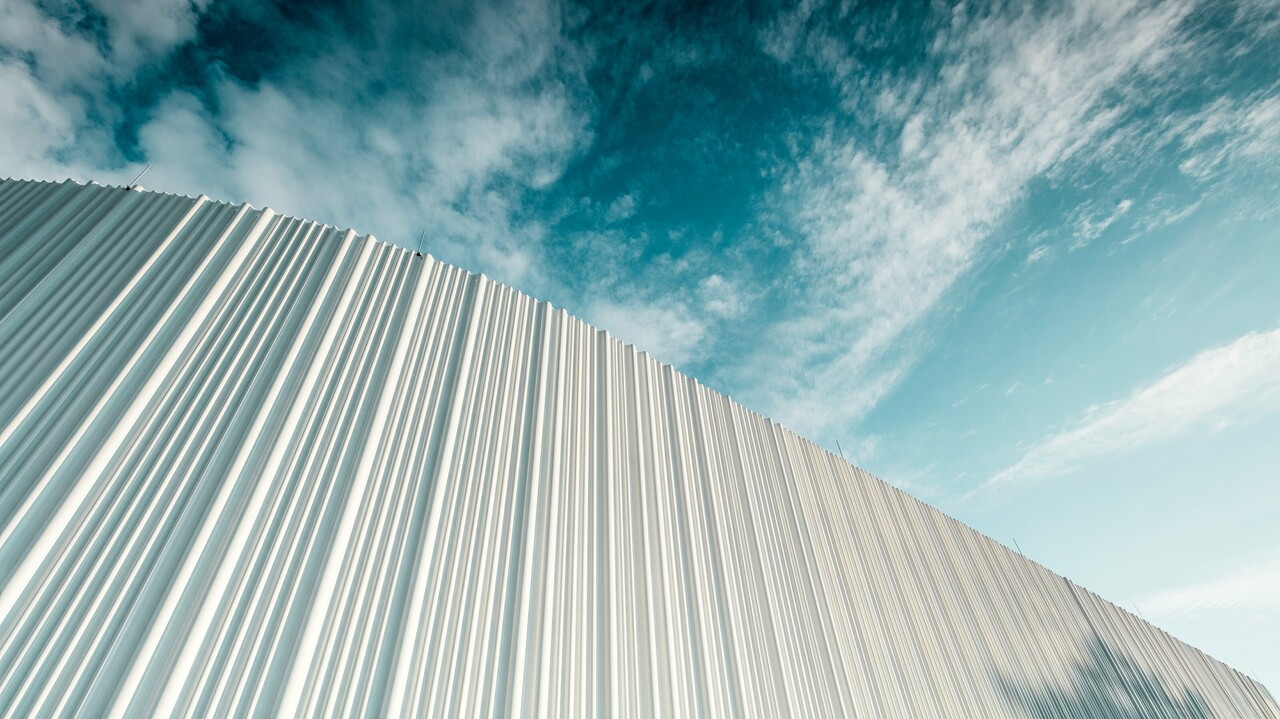 Atemberaubende Architektur mit weißer PREFA Aluminiumfassade im Walter Business-Park bei Wien. Die Fassade aus maßgefertigten Individualprofilen erzeugt durch ihren fließenden Wellencharakter ein faszinierendes Spiel aus Licht und Schatten. Drei unterschiedliche Profilformen sorgen für eine außergewöhnliche Tiefenwirkung und verleihen dem Gebäude eine stilistisch klare und zugleich dynamische Optik. Die langlebige, witterungsbeständige PREFA Oberfläche kombiniert moderne Ästhetik mit funktionaler Perfektion – ein echtes Highlight zeitgenössischer Fassadengestaltung, das architektonische Qualität und technische Raffinesse sichtbar macht.