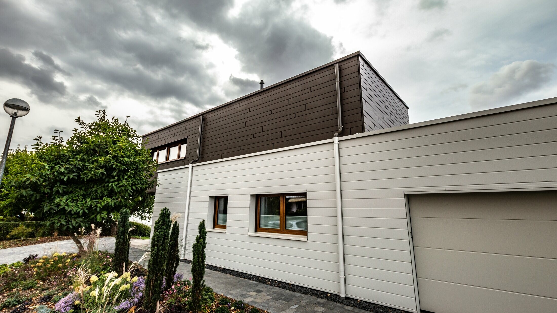 PREFA Siding Weiß braun Fassadengestaltung Garage Speiereinmündung Fassadenverkleidung einer Garage mit den PREFA Sidings horizonal in Weiß, mit Speiereinmündung.