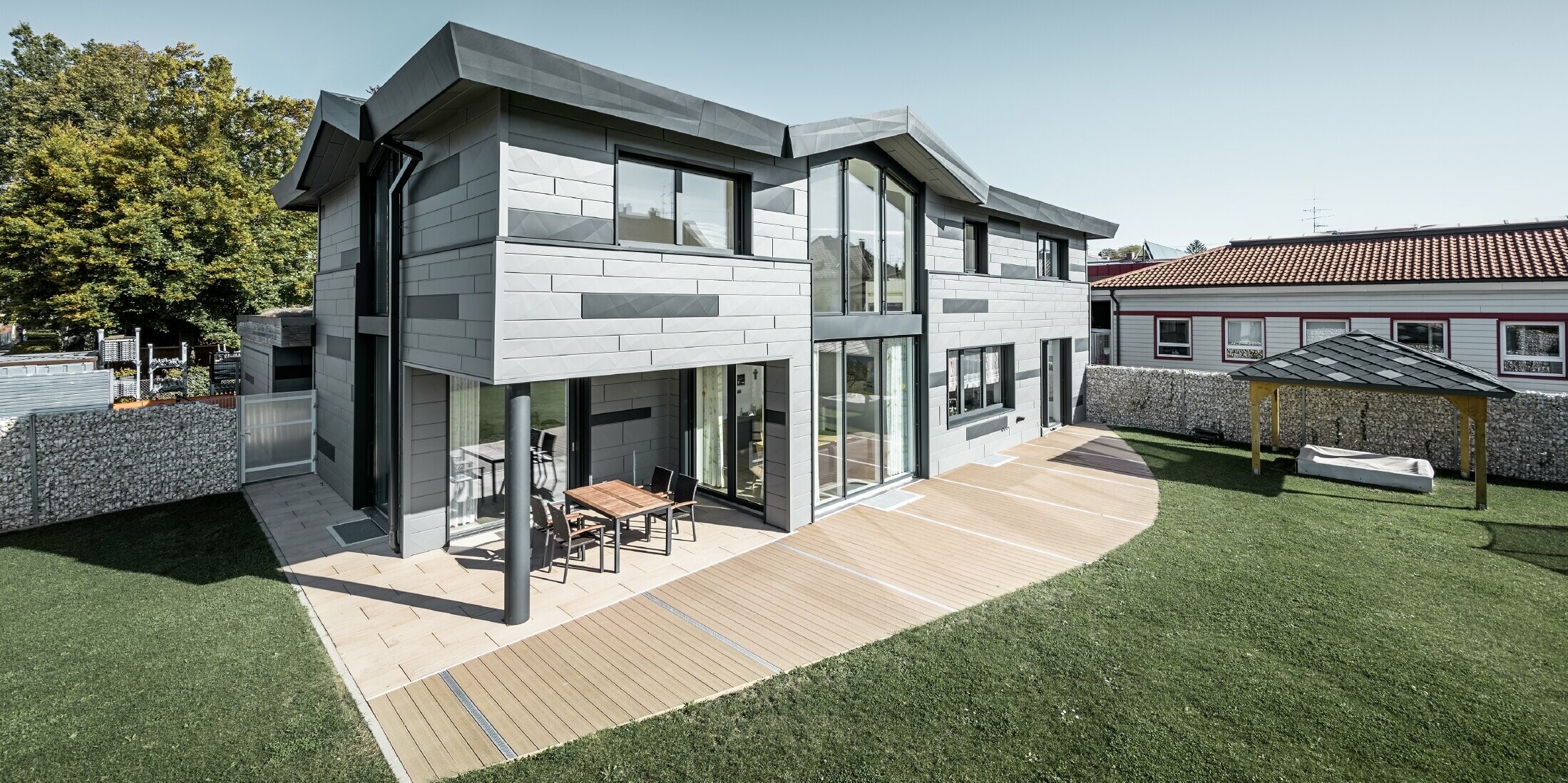 Das moderne Einfamilienhaus in Türkheim präsentiert die PREFA Fassadenpaneelen FX.12 in den Farben P.10 Hellgrau und Anthrazit. Das Bild zeigt einen Teil vom Garten.