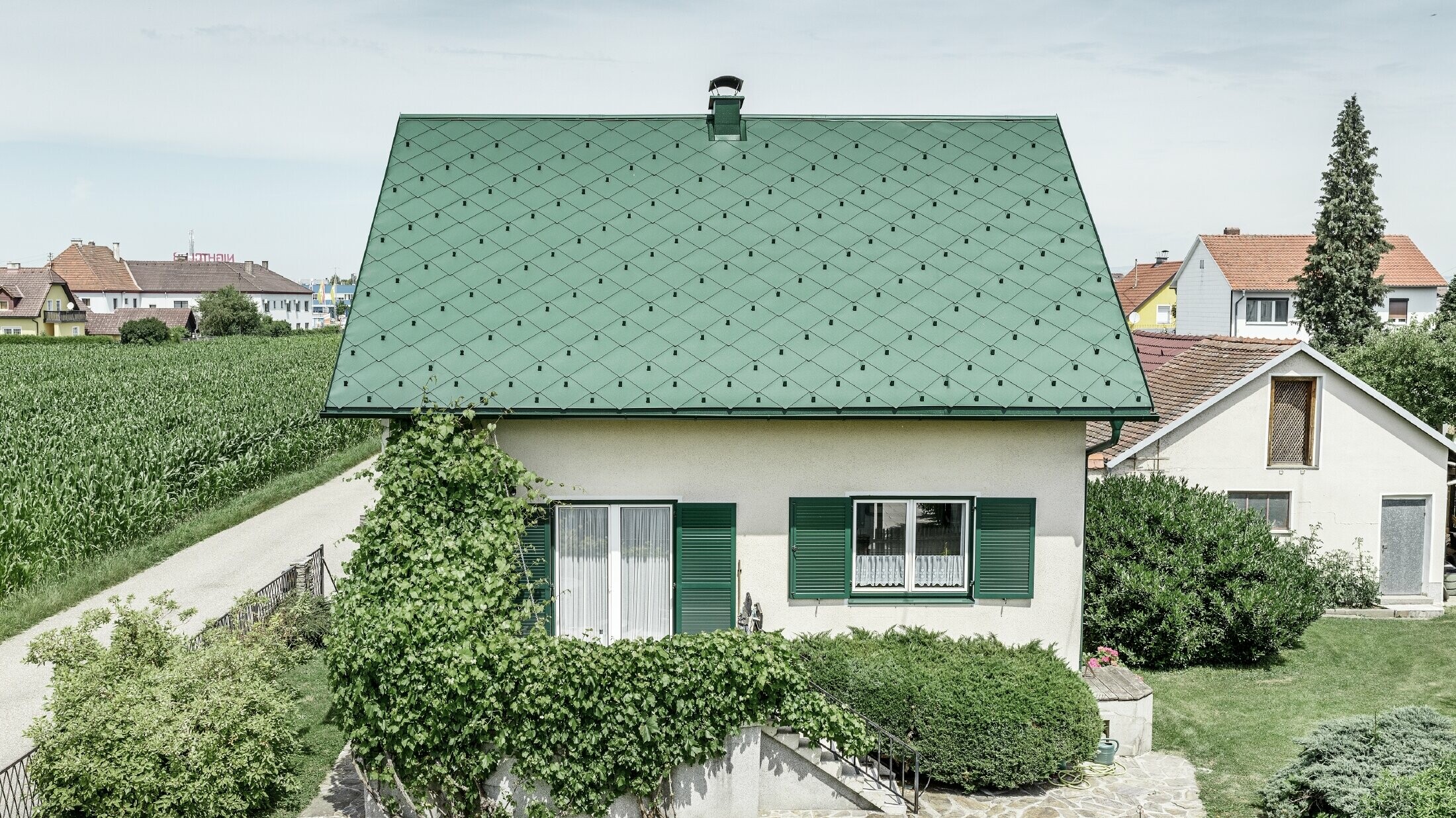 Klassisches Einfamilienhaus mit Satteldach mit einer Dacheindeckung aus Aluminium von in moosgrün mit grünen Fensterläden. Das Dach wurde mit PREFA Dachrauten 44 × 44 in P.10 Moosgrün eingedeckt.