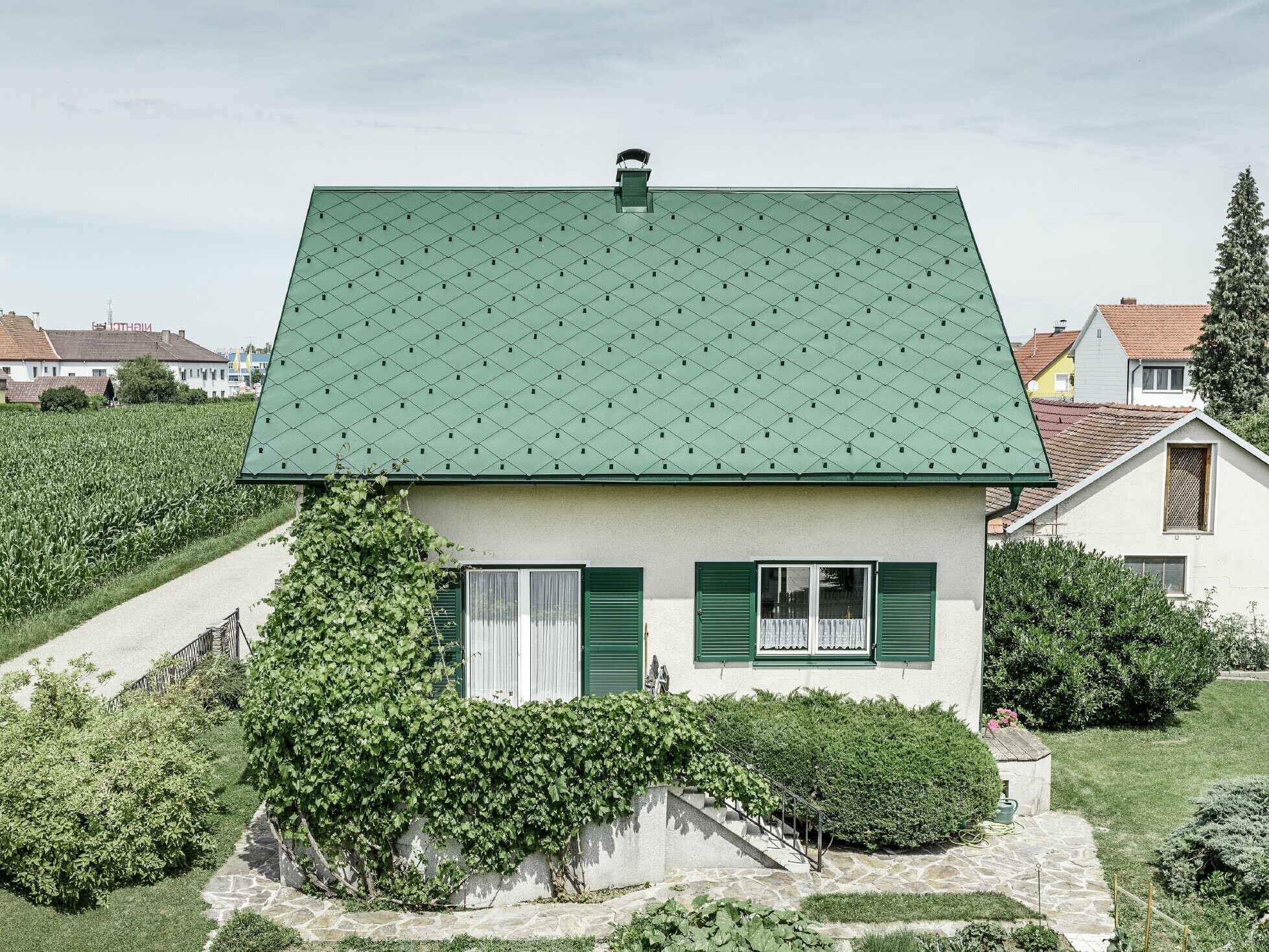 Klassisches Einfamilienhaus mit Satteldach mit einer Dacheindeckung aus Aluminium von in moosgrün mit grünen Fensterläden. Das Dach wurde mit PREFA Dachrauten 44 × 44 in P.10 Moosgrün eingedeckt.