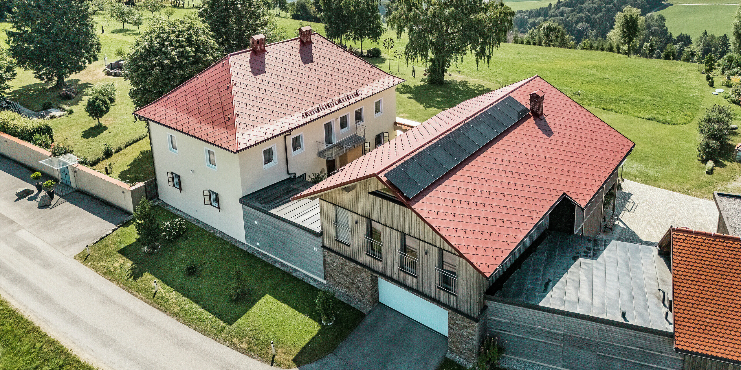 Bei einem Blick auf die sanierten Einfamilienhäuser in Aschachs an der Steyr fällt die markante PREFA Dachraute 44 x 44 in der Farbe P.10 Oxydrot sofort ins Auge. Die kräftige rote Farbe der Aluminiumdächer harmoniert perfekt mit der umliegenden Natur und fügt sich nahtlos in das idyllische Bergpanorama ein.